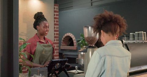 African american barista serving customer at coffee shop counter with espresso machine