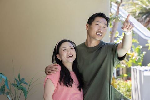 Asian couple enjoying sunny balcony view, pointing and smiling together