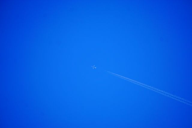 Airplane flying high in clear blue sky, creating contrail. Perfect for illustrating concepts related to aviation, travel, transportation, and meteorology. Ideal for use in travel blogs, educational materials, aviation websites, and weather-related publications.