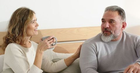 Middle-Aged Couple Sharing Cozy Morning Conversation on Sofa with Coffee and Knitwear