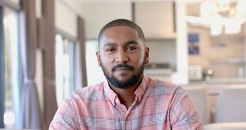 Calm african american man sitting at kitchen table wearing plaid shirt casual portrait