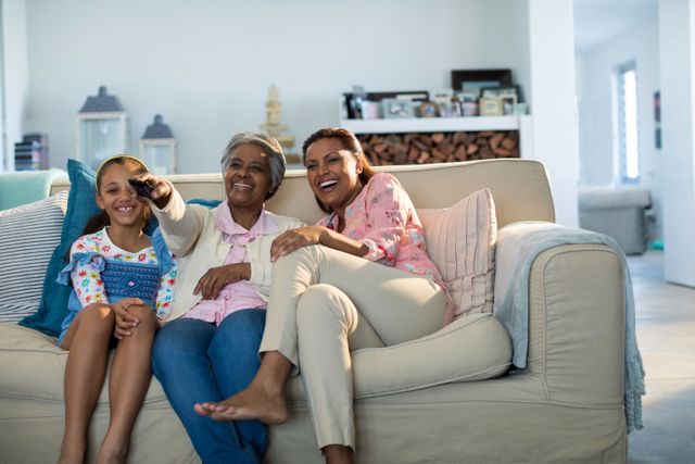 This image captures a joyful moment of a multigenerational family watching television together in a cozy living room. Ideal for use in advertisements, articles, or blog posts about family bonding, home life, and leisure activities. It can also be used in promotional materials for family-oriented products and services.