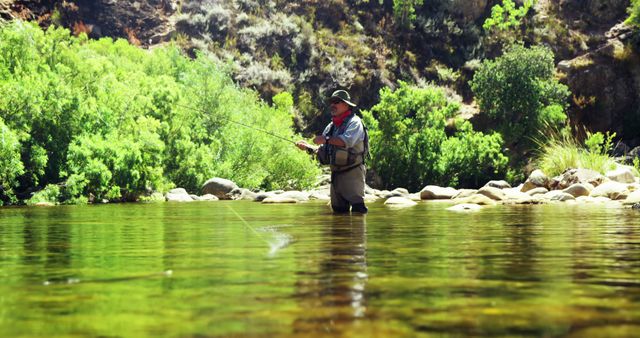 Man engaged in fly fishing in clear mountain stream surrounded by lush greenery. Ideal for use in blogs, articles, or advertisements related to outdoor activities, adventure sports, nature travel, and peaceful retreats.