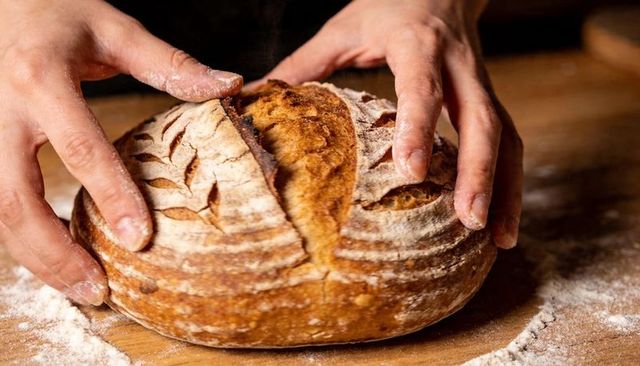 Hands shaping sourdough loaf on wooden board with flour dusting and crust detail