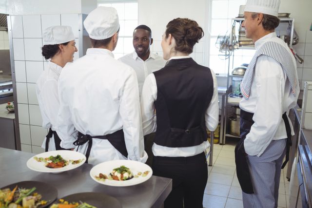 Restaurant manager briefing kitchen staff in commercial kitchen, ideal for content on teamwork, hospitality industry, culinary team coordination, and restaurant operations. Suitable for articles, blog posts, and marketing materials related to restaurant management and employee engagement.