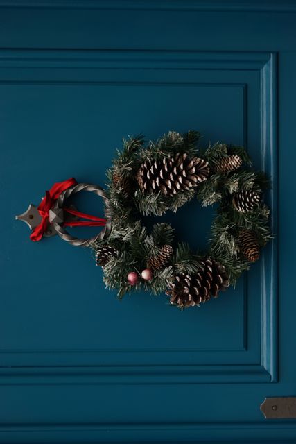 Festive Christmas wreath hanging on blue wooden door, decorated with pine cones and red ribbon, evokes traditional holiday charm. Use for seasonal home decor ideas, Christmas greeting cards, holiday advertisements, blog posts, or as inspiration for festive decorating tips.