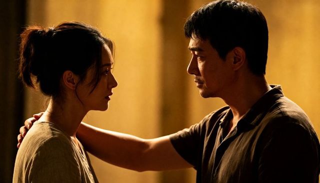 Intimate gaze between couple in warm golden room, man resting hand on shoulder
