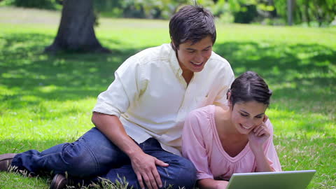 Happy Couple Using Laptop Outdoors on Sunny Day