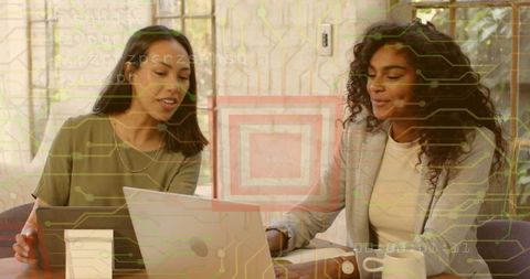 Two women collaborating over laptop and tablet in modern tech-focused coworking workspace