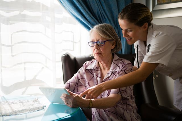 Female doctor assisting elderly woman with digital tablet in nursing home. Ideal for illustrating healthcare, senior care, and technology use among elderly. Useful for articles on elderly support, medical assistance, and digital literacy for seniors.