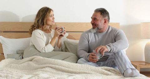Middle-aged couple sharing morning coffee in cozy bedroom, relaxed conversation