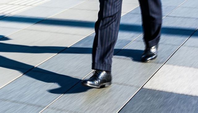 Businessman walking on urban plaza with polished black shoes and navy pinstripe trousers