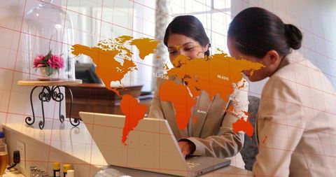 Two businesswomen collaborating on laptop with orange map overlay for global planning