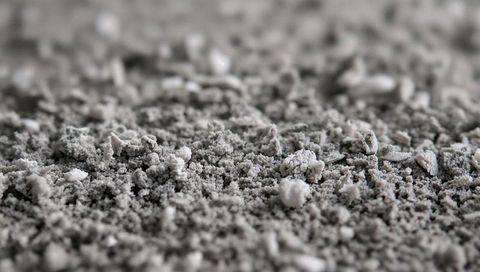 Macro gray granular powder texture with small clumps and white pellets, abstract surface
