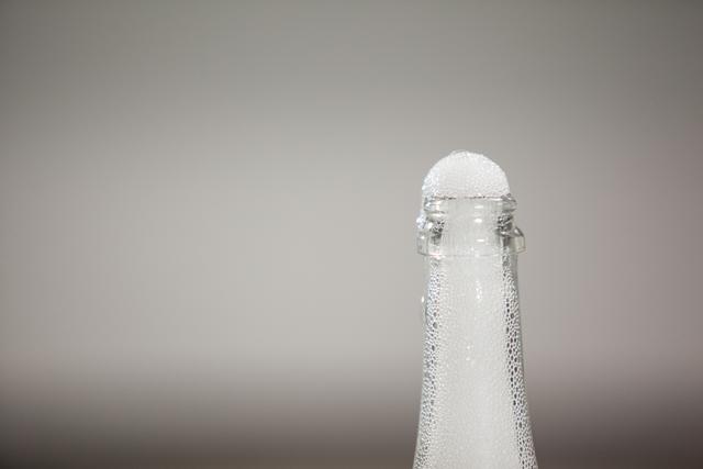 Close-up of froth flowing out of champagne bottle against gray background