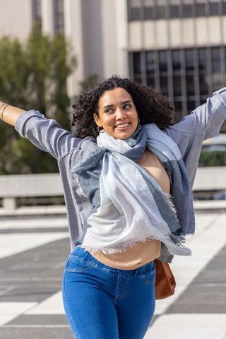 Young woman celebrating on urban rooftop plaza, scarf fluttering, arms wide in breeze
