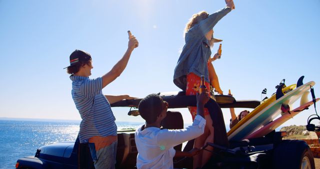 Young friends on a road trip are celebrating near the ocean with surfboards and drinks. They are on a convertible car, enjoying themselves under the bright sun. Perfect for use in travel blogs, advertisements for summer vacations, youth activities, and lifestyle promotions.