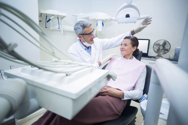 Dentist engaging in conversation with patient in modern dental clinic. Ideal for use in healthcare, dental care, and medical consultation contexts. Suitable for illustrating professional dental services, patient care, and oral health education.