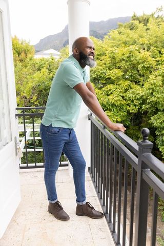 African american man leaning on balcony railing overlooking lush garden and mountain view