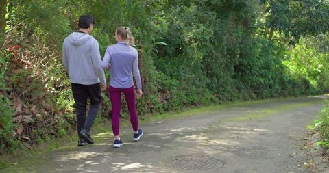 Couple walking along shaded forest lane during casual outdoor exercise and nature stroll