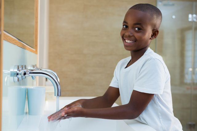This image shows a young boy smiling while washing his hands in a bathroom sink. It can be used to promote hygiene practices, health awareness, and personal care routines. Ideal for educational materials, health campaigns, and family-oriented content.
