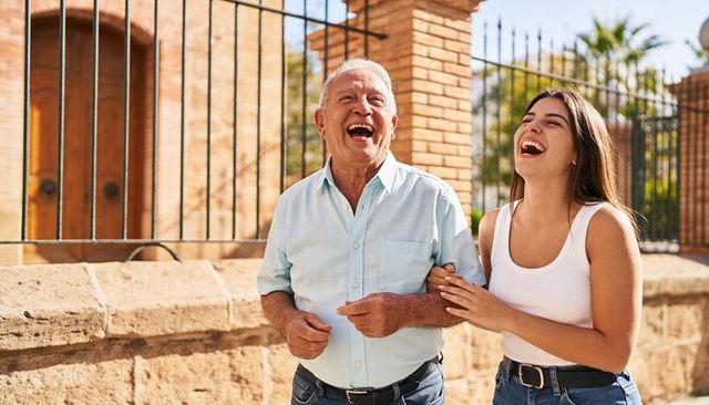Senior man and adult woman walking and laughing together in sunlit courtyard with brick architecture