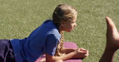 Young girl lying on yoga mat in sunny park practicing relaxation and barefoot play for child wellnes