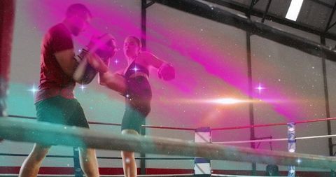 Female kickboxer practicing high kick with coach holding focus pads in boxing ring