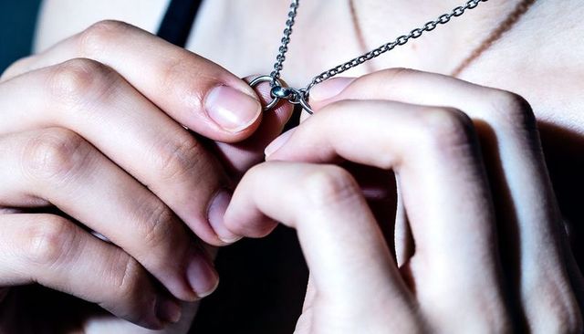 Close-up hands holding silver chain clasp revealing linked rings at collarbone