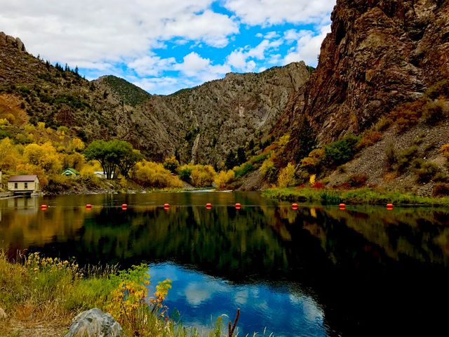 This scenic image showcases a tranquil lake surrounded by rugged rocky mountains and vibrant autumn foliage. The reflective water and bright sky enhance the natural beauty of the location. Ideal for nature-themed blogs, travel articles, outdoor adventure promotions, and wallpaper for computers or mobile devices.