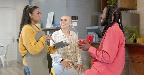 Barista talking with customers at cafe counter while showing tablet, coffee conversation