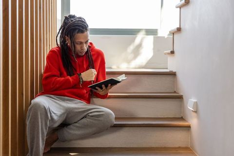 African american man journaling on sunlit staircase wearing red hoodie