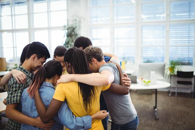 Group of diverse business executives forming a huddle in an office environment, showing unity and teamwork. Ideal for illustrating concepts of collaboration, team spirit, and workplace support. Suitable for use in business presentations, team-building materials, and corporate websites.
