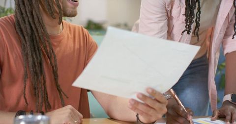 African American coworkers reviewing documents and annotating chart at wooden table