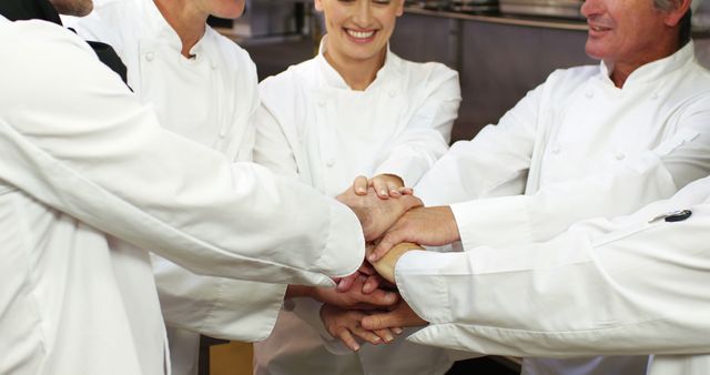 Chefs uniting hands in commercial kitchen. This image captures the spirit of cooperation and teamwork among culinary professionals, and is suitable for illustrating themes of collaboration, support, and unity in restaurant or hospitality industry. This could be used in advertisements, team-building presentations, or promotional materials for culinary schools.