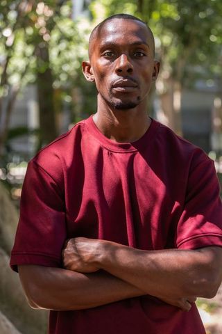 African american man standing with arms crossed in park wearing burgundy t-shirt