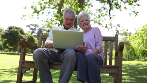 Seniors Smiling While Using Laptop in Park