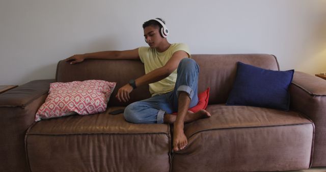 Biracial man wearing headphones sitting on sofa using smartphone and smiling. staying at home in isolation during quarantine lockdown.
