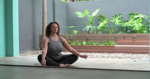 African american woman meditating on patio yoga mat surrounded by tropical greenery serene