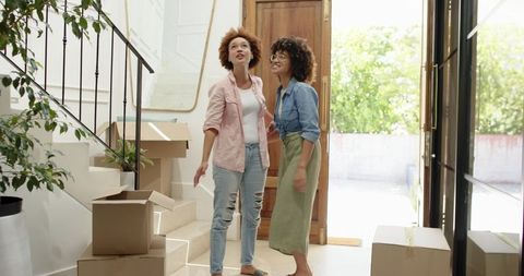 African American Friends Unpacking New Home Inspecting Staircase in Bright Foyer