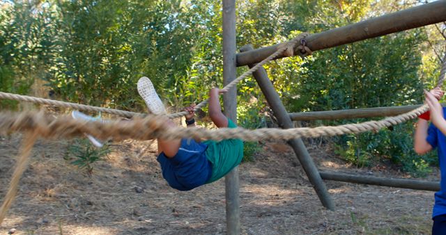 Child engaging in a physical activity in an outdoor adventure park, climbing on a rope obstacle set in a lush green forest environment. Ideal for use in marketing materials for outdoor recreation courses, adventure parks, summer camps, or featuring in articles about active lifestyles for children and outdoor adventures.