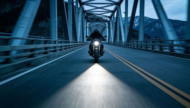 Dusk motorcycle rider crossing steel truss bridge, headlight cutting moody blue highway
