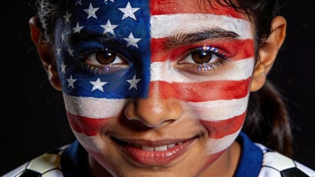 Smiling child wearing american flag face paint with glitter eyes and soccer collar closeup