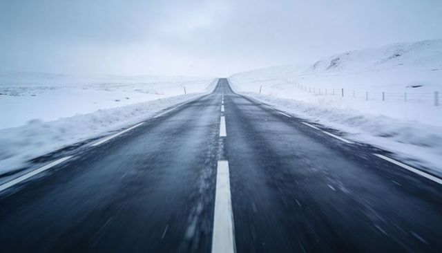 Empty snow-covered road leading toward horizon through minimalist winter landscape