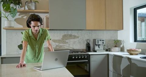 Adult man working on laptop in modern minimalist kitchen leaning on marble island