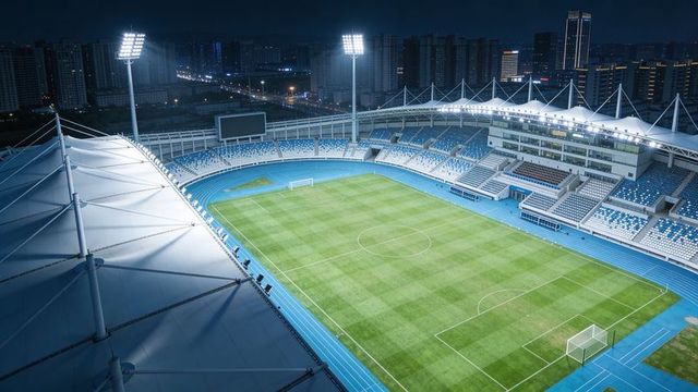 Modern stadium glowing under floodlights with green pitch and blue running track at night