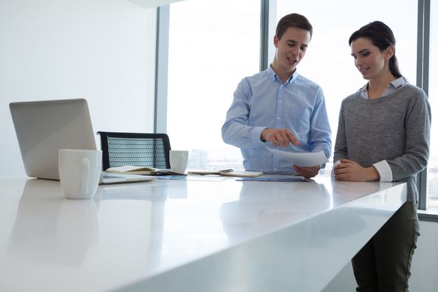 Male executive and female executive discussing over document in futuristic  office