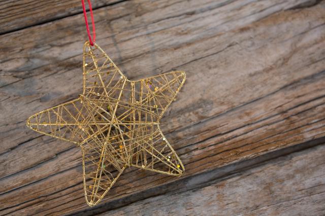Golden star ornament hanging against a rustic wooden background, perfect for holiday-themed designs, Christmas cards, festive decorations, and seasonal promotions. The handmade look adds a touch of traditional charm, making it ideal for craft and DIY project inspirations.