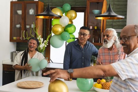 Multiethnic friends decorating kitchen with green and gold balloons, sharing laughter