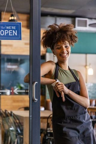 African american barista smiling and adjusting watch while opening coffeehouse door